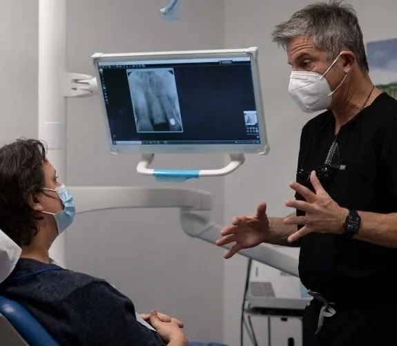 A dentist explaining a digital x-ray on a chairside screen to a patient.